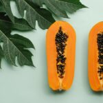 Top view of freshly halved papayas with leafy background, highlighting tropical freshness.