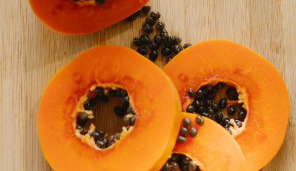 Top view of fresh, ripe papaya slices with seeds on a wooden board, showcasing vibrant tropical fruit.