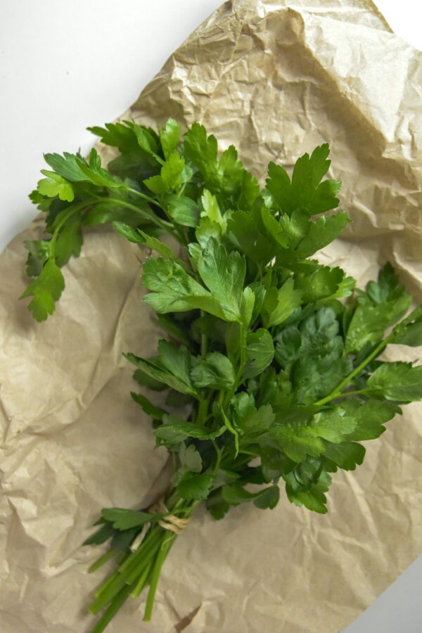Bunch of fresh parsley placed on crumpled brown paper, perfect for culinary or herb-themed photography.