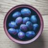 Top view of fresh organic plums in a rustic bowl on a wooden table, perfect for healthy diet themes.