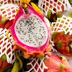 Close-up of sliced dragon fruit with netted fruit in background, highlighting tropical colors and textures.